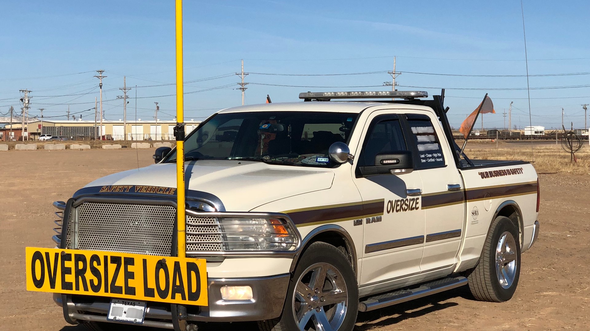 Cream oversize-load safety vehicle with yellow high pole and OVERSIZE LOAD bumper sign